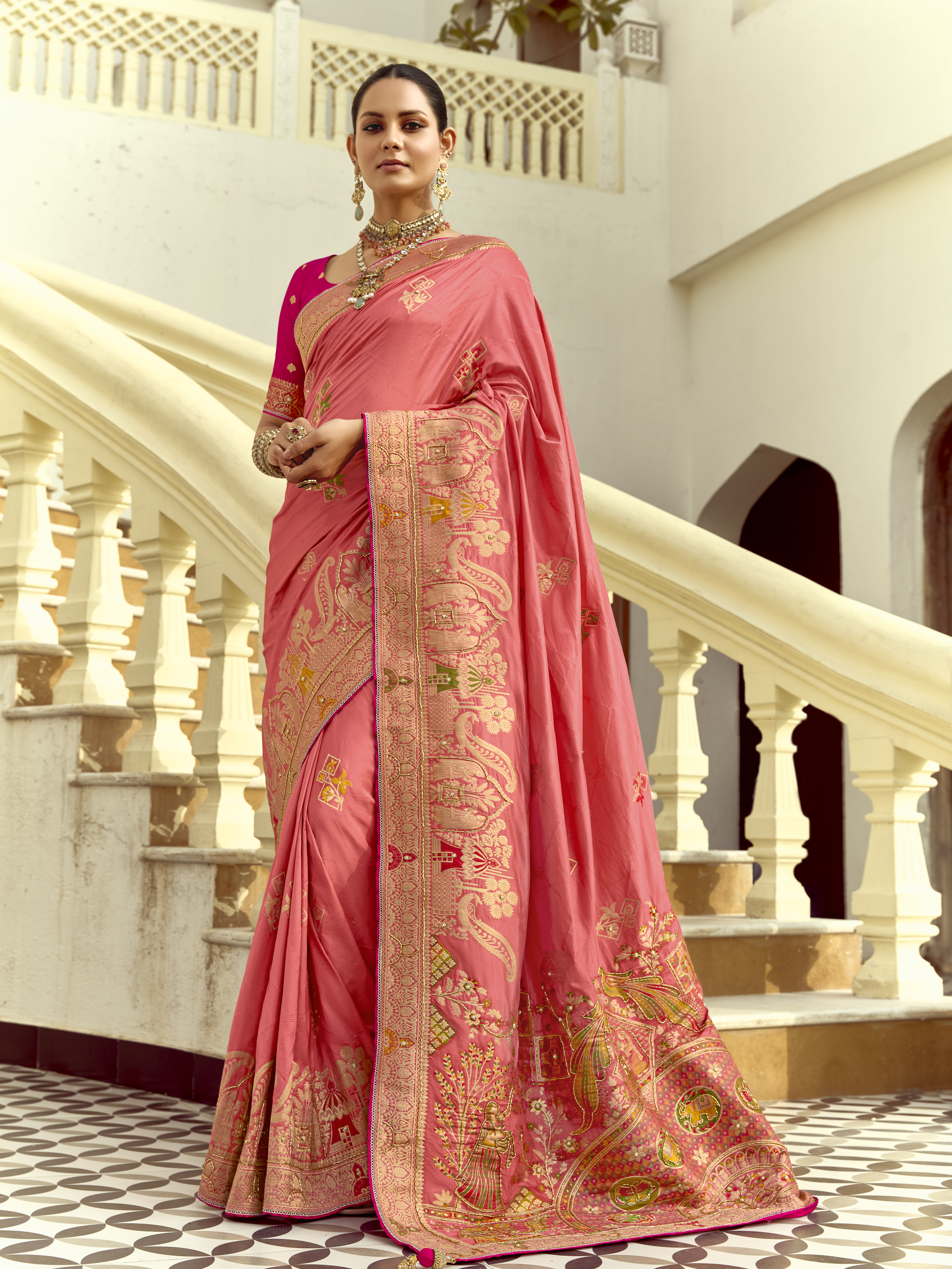 Woman wearing a pink saree with intricate designs in an elegant indoor setting.