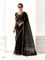 Woman wearing a black saree with white patterns against a light-colored wall.