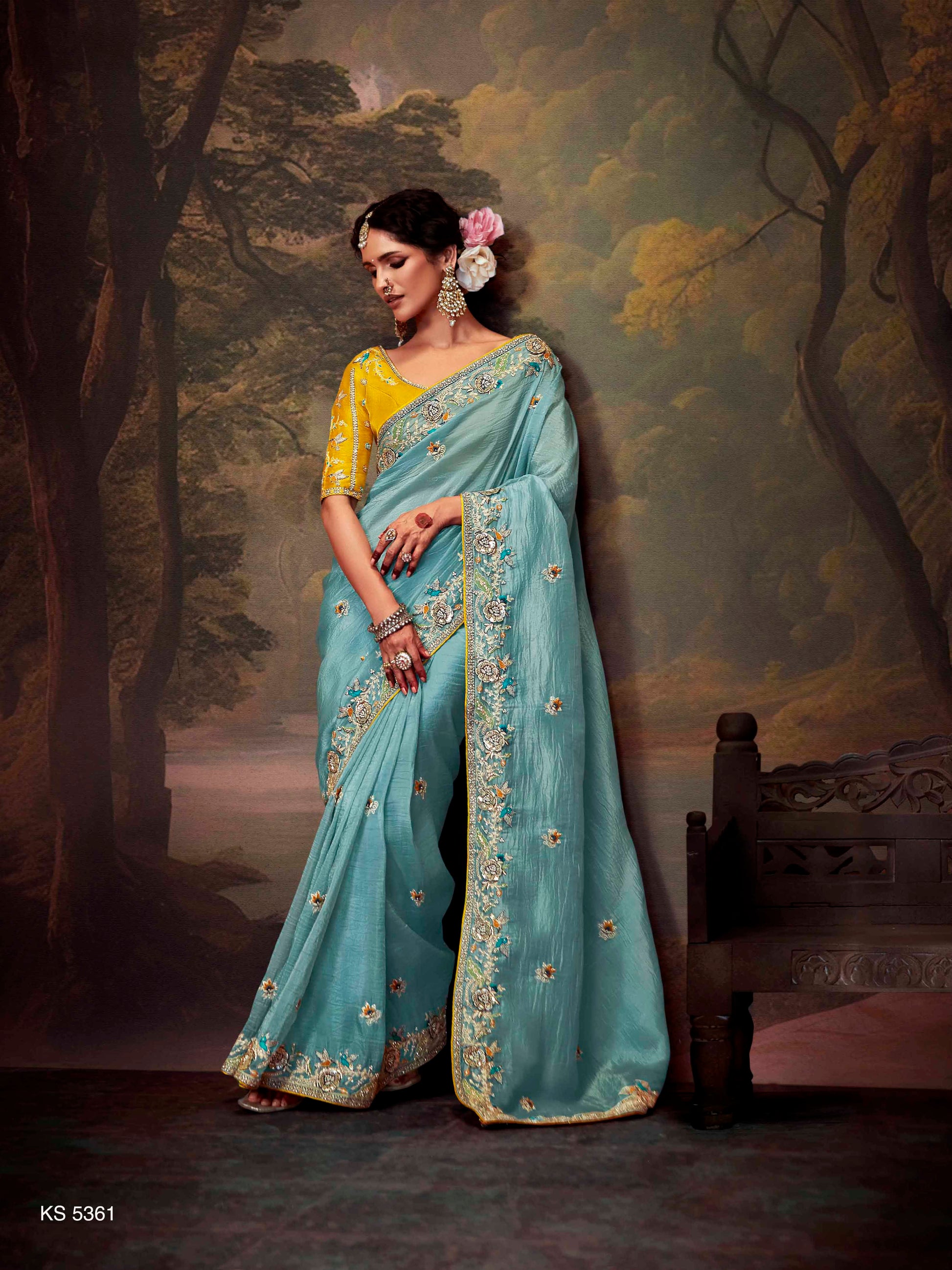 Woman in a light blue saree with yellow blouse against a scenic backdrop