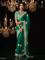 Woman in a green saree with floral patterns standing under chandeliers