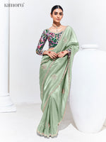 Woman wearing a light green saree with floral blouse against a white background