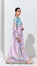 Woman wearing a light purple saree with a colorful blouse against a white background