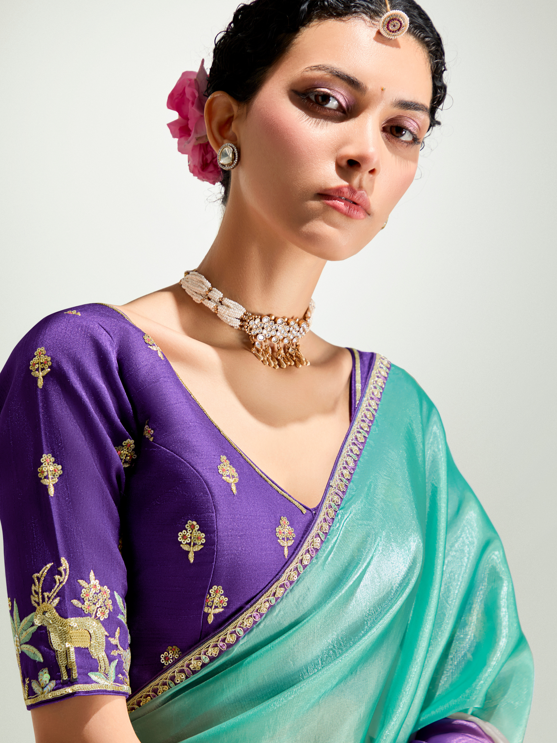 Woman wearing a purple and green saree with gold embroidery on a white background