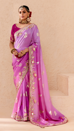 Woman wearing a pink saree with gold embroidery on a beige background