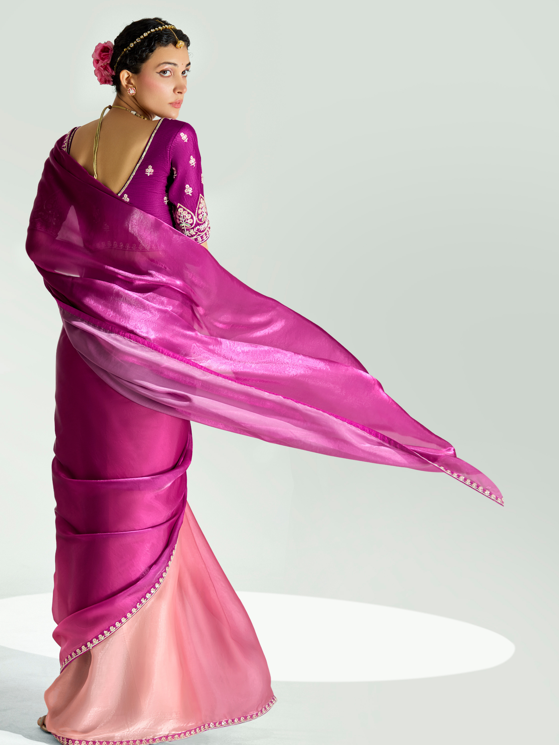 Woman wearing a vibrant pink saree with a white blouse against a plain background
