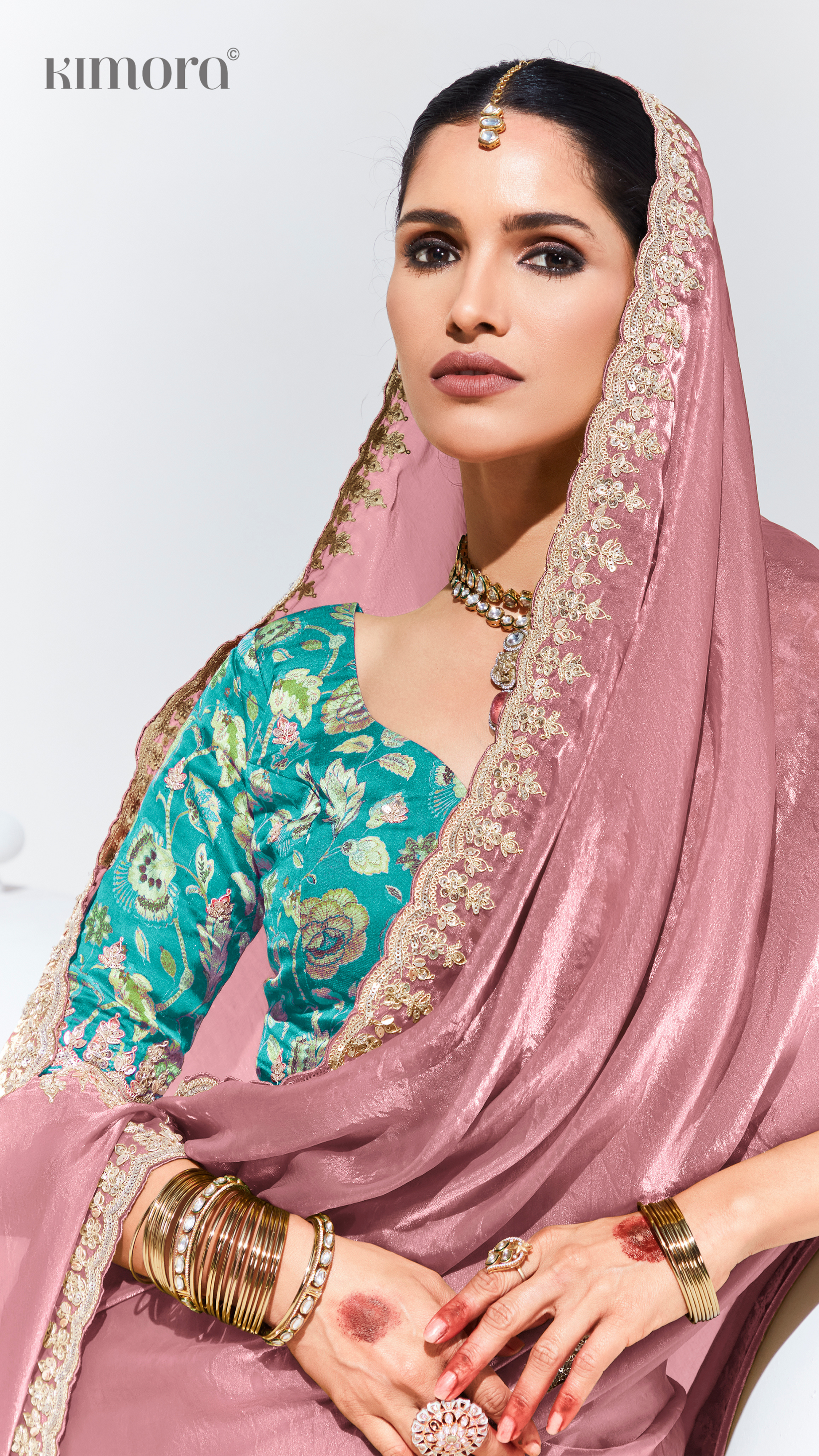Woman wearing a traditional outfit with a pink dupatta and teal blouse against a white background