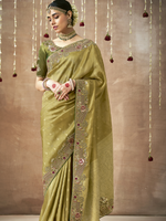 Woman wearing a green saree with intricate patterns against a brown background