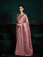 Woman wearing a pink saree with gold patterns against a dark background