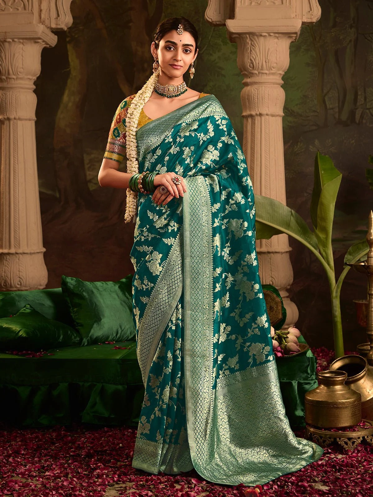 Woman in a green saree with white patterns standing in an ornate setting.