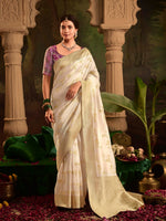 Woman in a white saree with a purple blouse standing in an ornate setting.