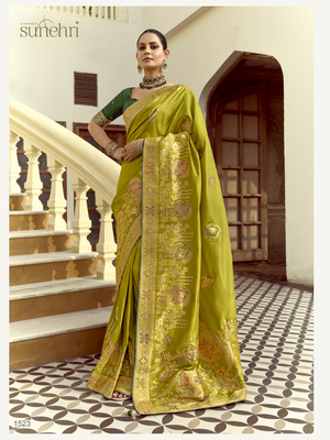 Woman in a green saree with gold patterns standing in an elegant interior setting.