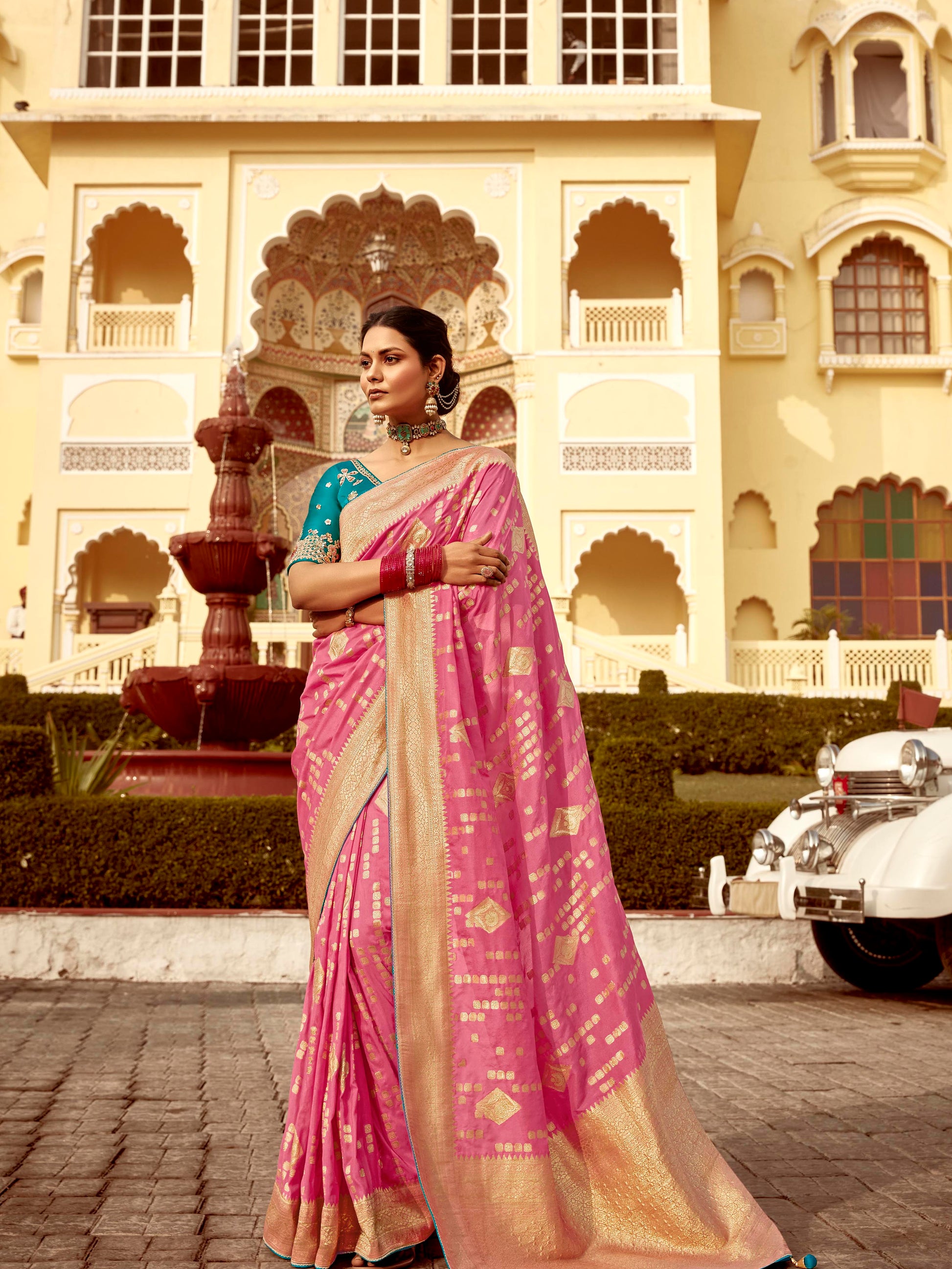 Woman in a pink saree standing in front of an ornate building.