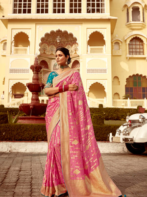 Woman in a pink saree standing in front of an ornate building.