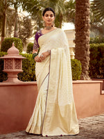 Woman in a white saree standing outdoors with greenery in the background
