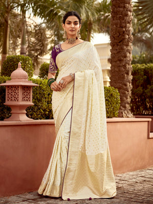 Woman in a white saree standing outdoors with greenery in the background