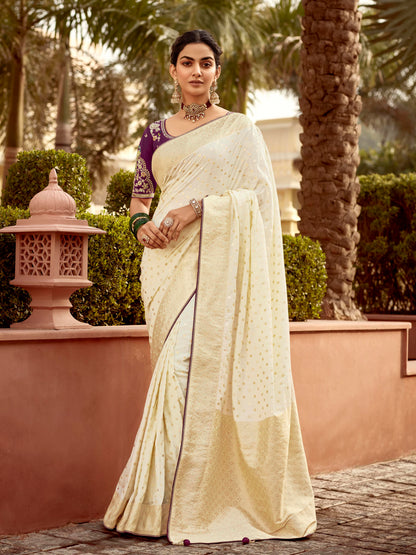 Woman in a white saree standing outdoors with greenery in the background