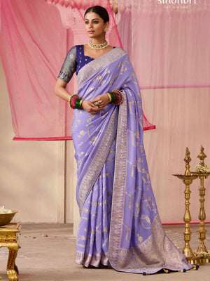 Woman wearing a lavender saree with a gold border in a decorated room.