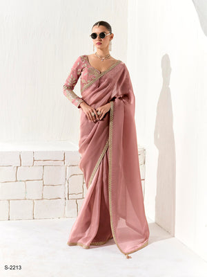 Woman wearing a pink saree with gold border against a white background, brand 'kimora' visible.