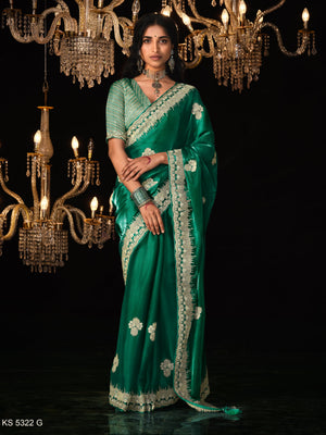 Woman in a green saree with floral patterns standing under chandeliers