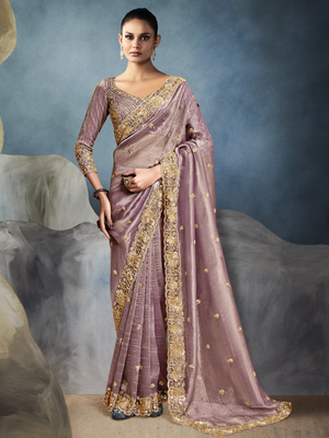 Woman wearing a mauve saree with gold embroidery against a textured gray background