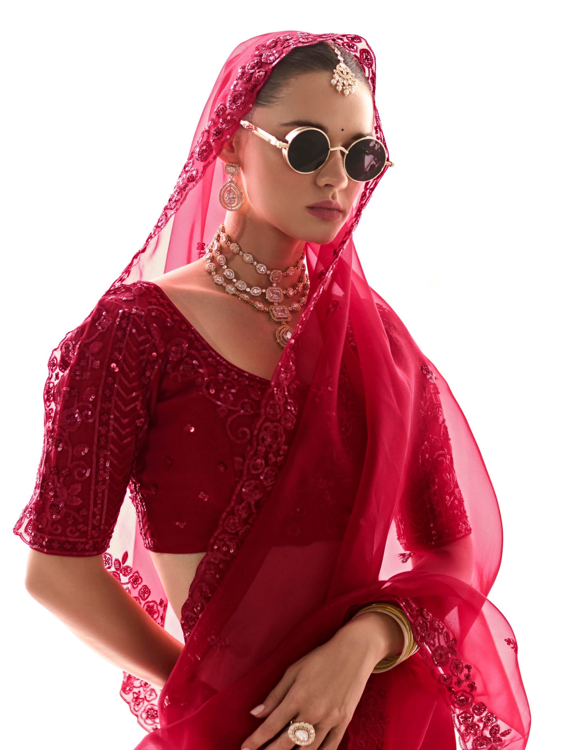 Woman wearing a red embroidered saree with sunglasses and jewelry on a white background