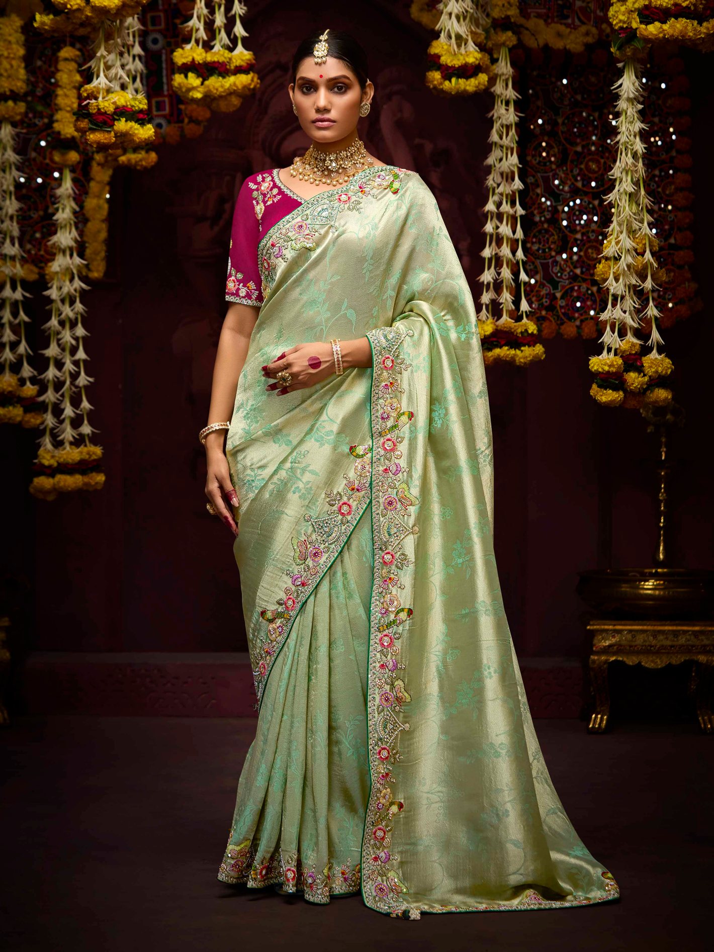 Woman wearing a light green saree with floral patterns against a decorated backdrop