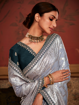Woman wearing a traditional saree with intricate patterns and jewelry against a warm-toned background
