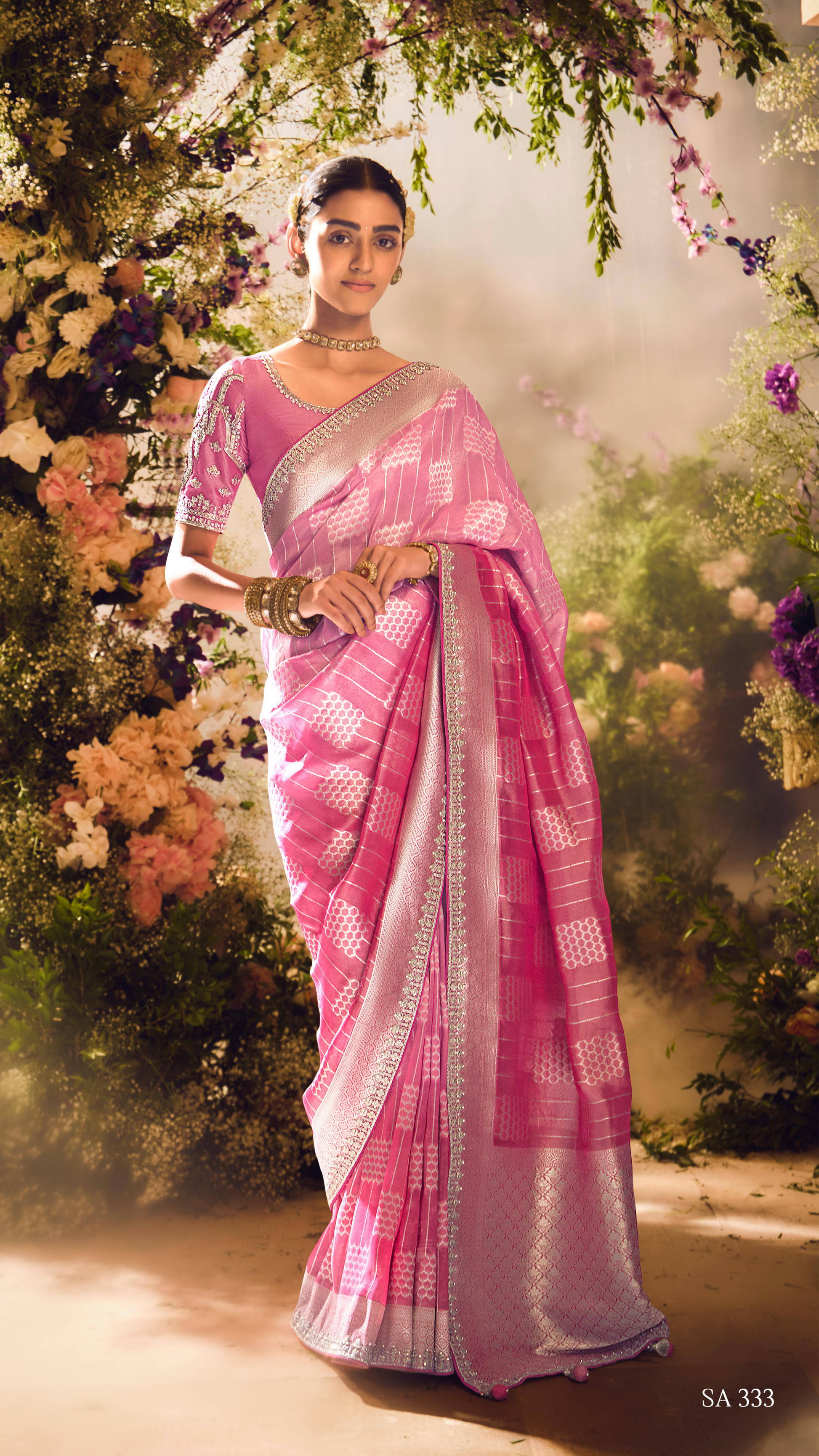 Woman in a pink saree standing among flowers and greenery