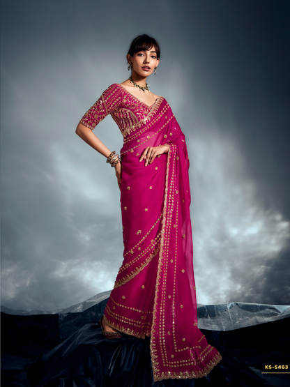 Woman wearing a pink saree with gold embroidery against a dark background