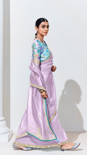 Woman wearing a light purple saree with a colorful blouse against a white background