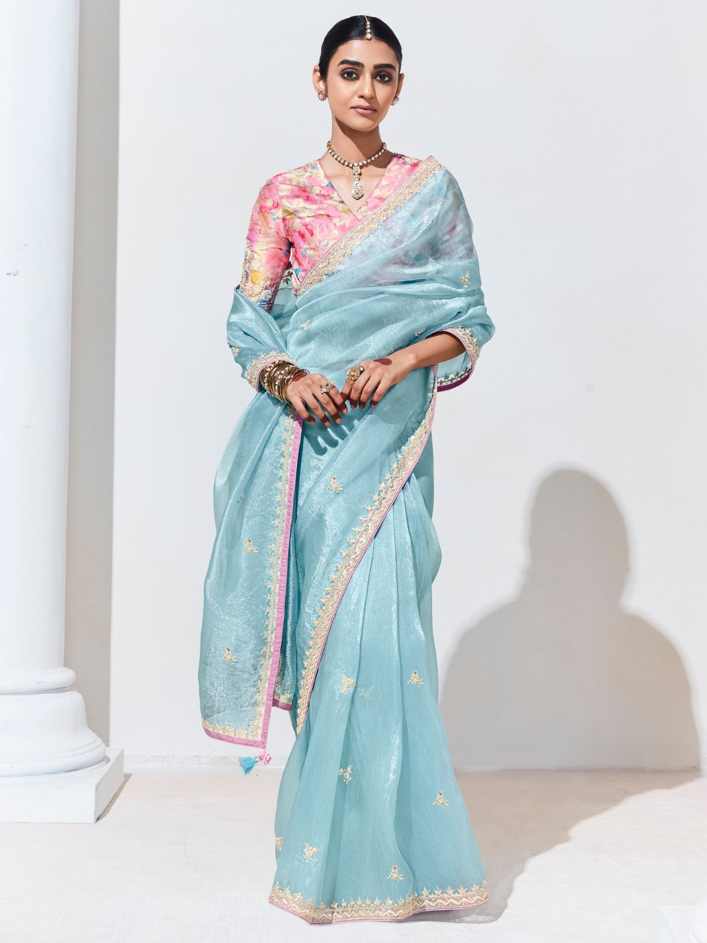 Woman wearing a light blue saree with a pink blouse against a white background