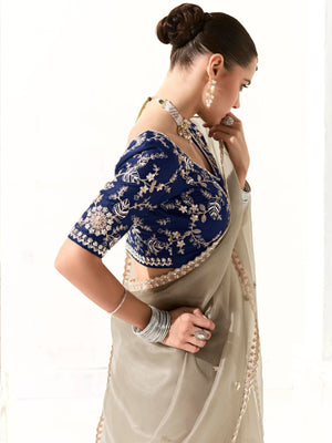 Woman wearing a blue embroidered blouse with a beige saree on a white background