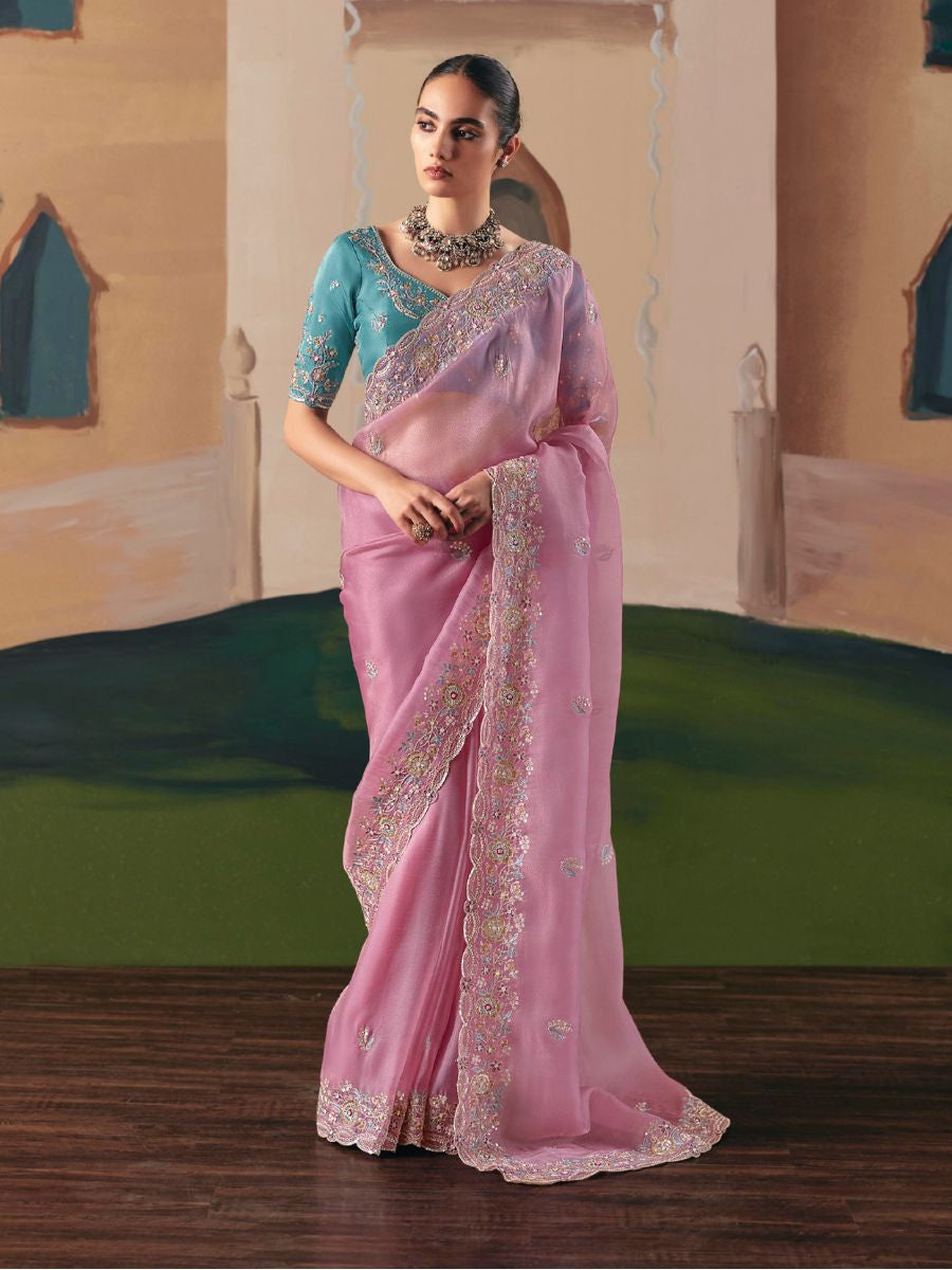 Woman wearing a pink saree with a blue blouse in an indoor setting.