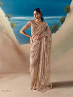 Woman in a beige saree standing against a desert landscape with blue sky.
