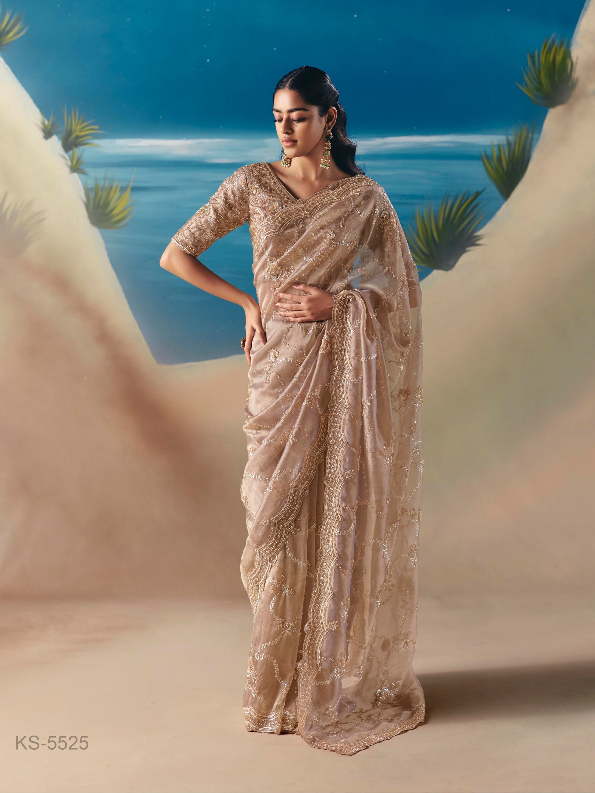 Woman in a beige saree standing against a desert landscape with blue sky.