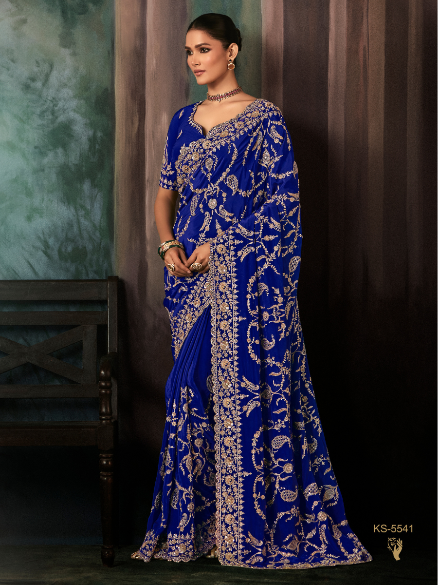 Woman wearing a blue saree with white patterns against a dark background