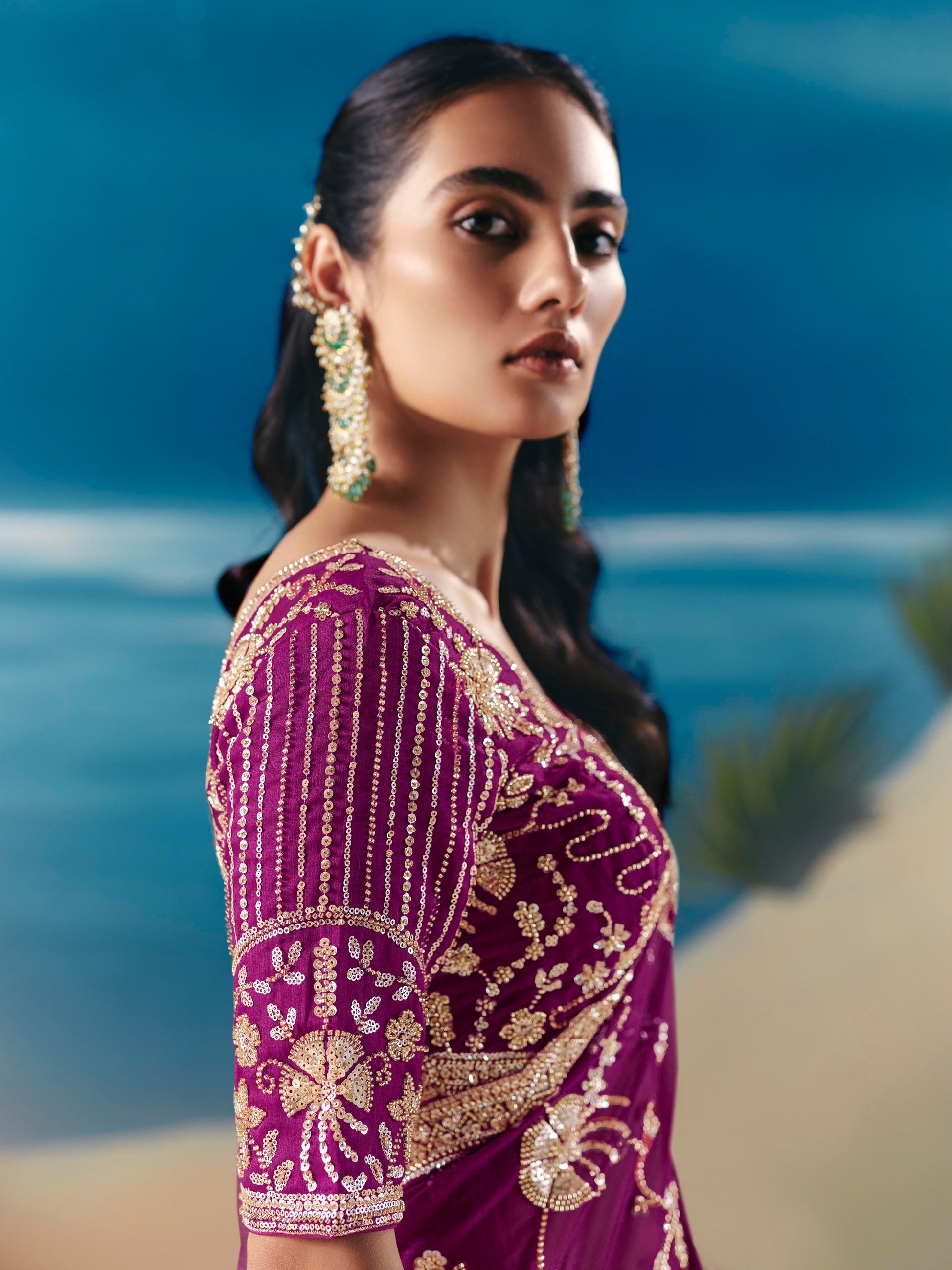 Woman wearing a purple saree with gold embroidery against a blurred natural background