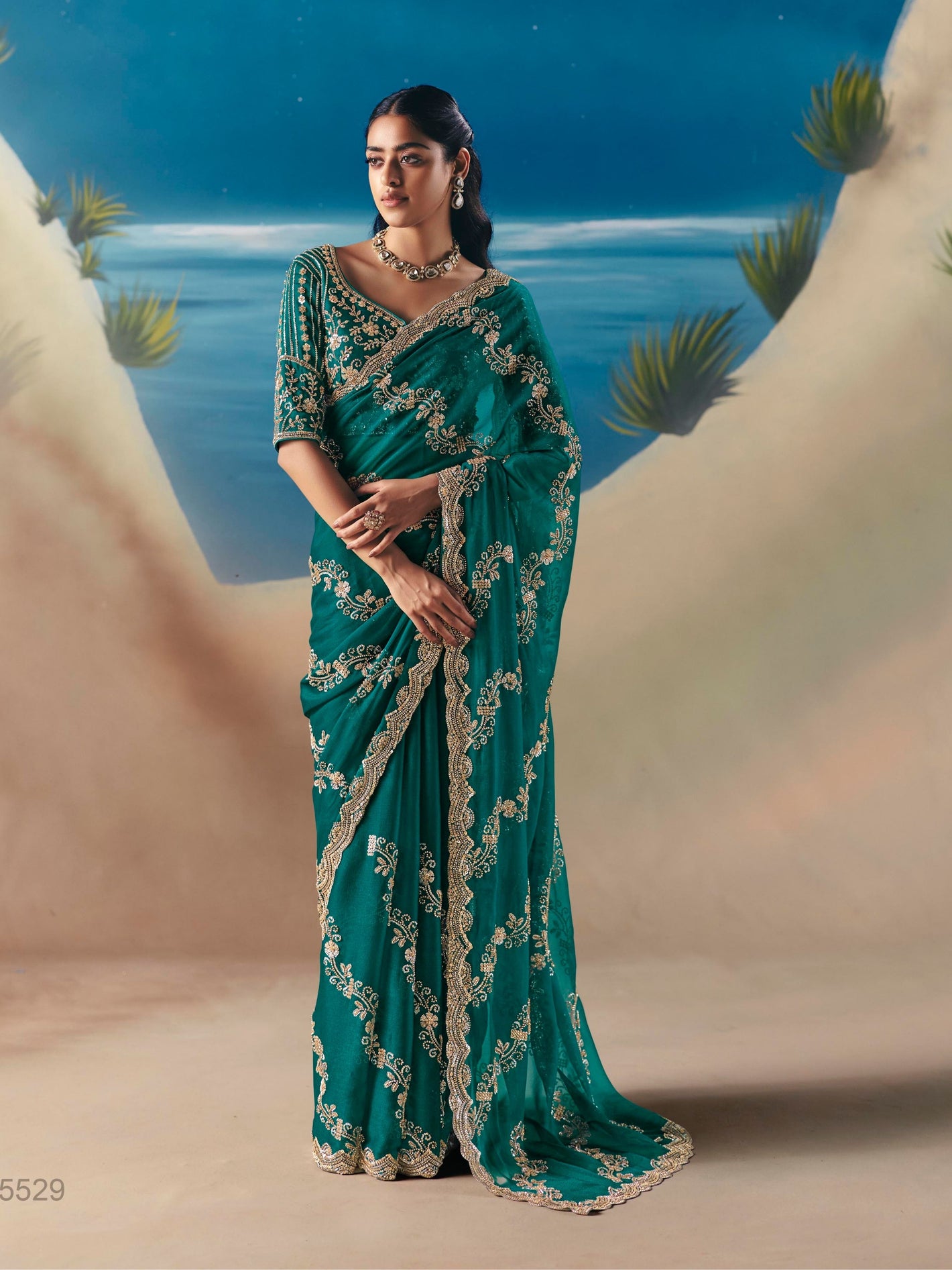 Woman in a teal saree with gold embroidery against a scenic background