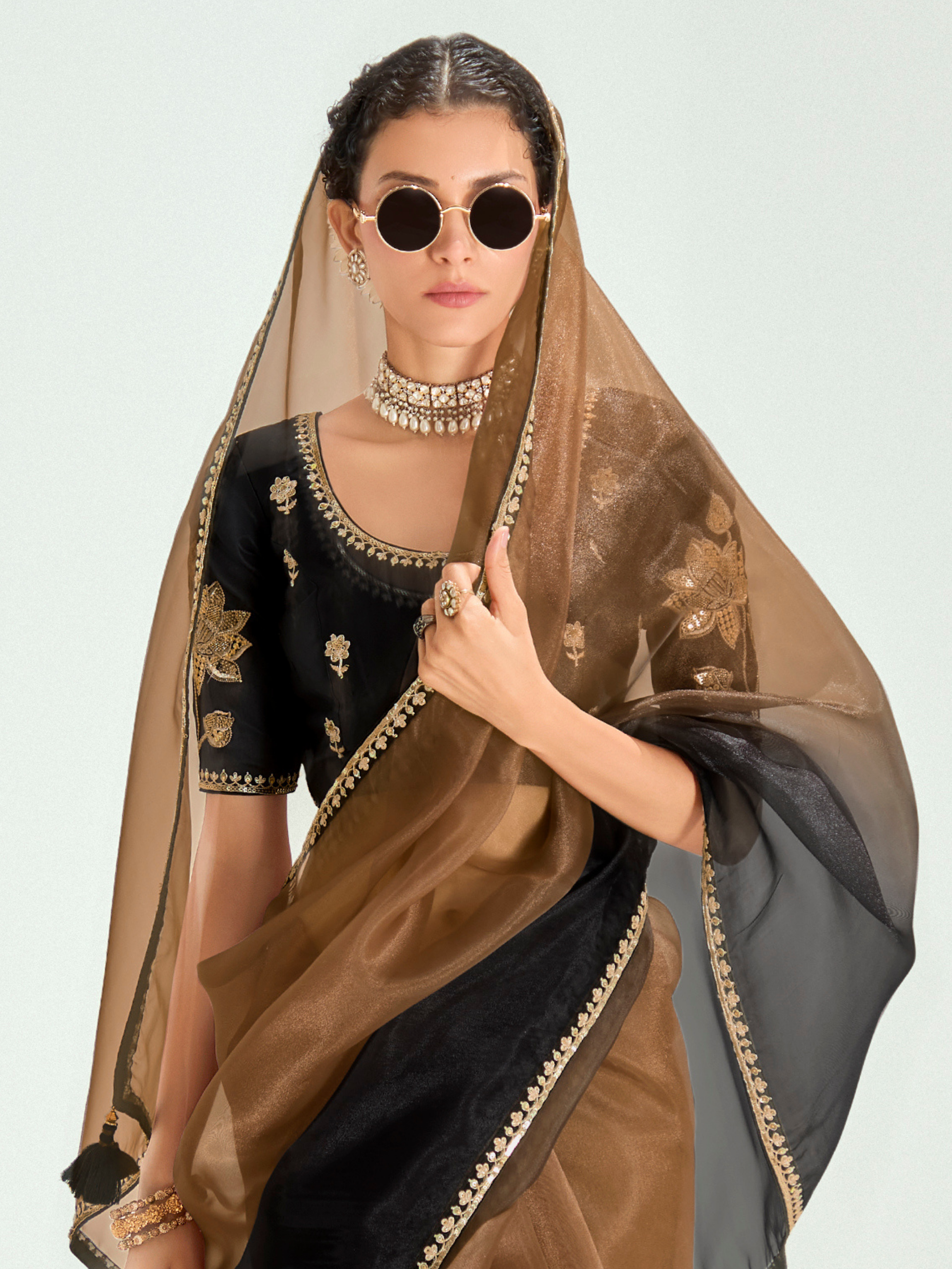 Woman wearing a black and gold embroidered blouse with a brown dupatta against a light gray background