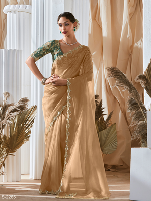 Woman in a beige saree with green blouse standing in a decorated room.