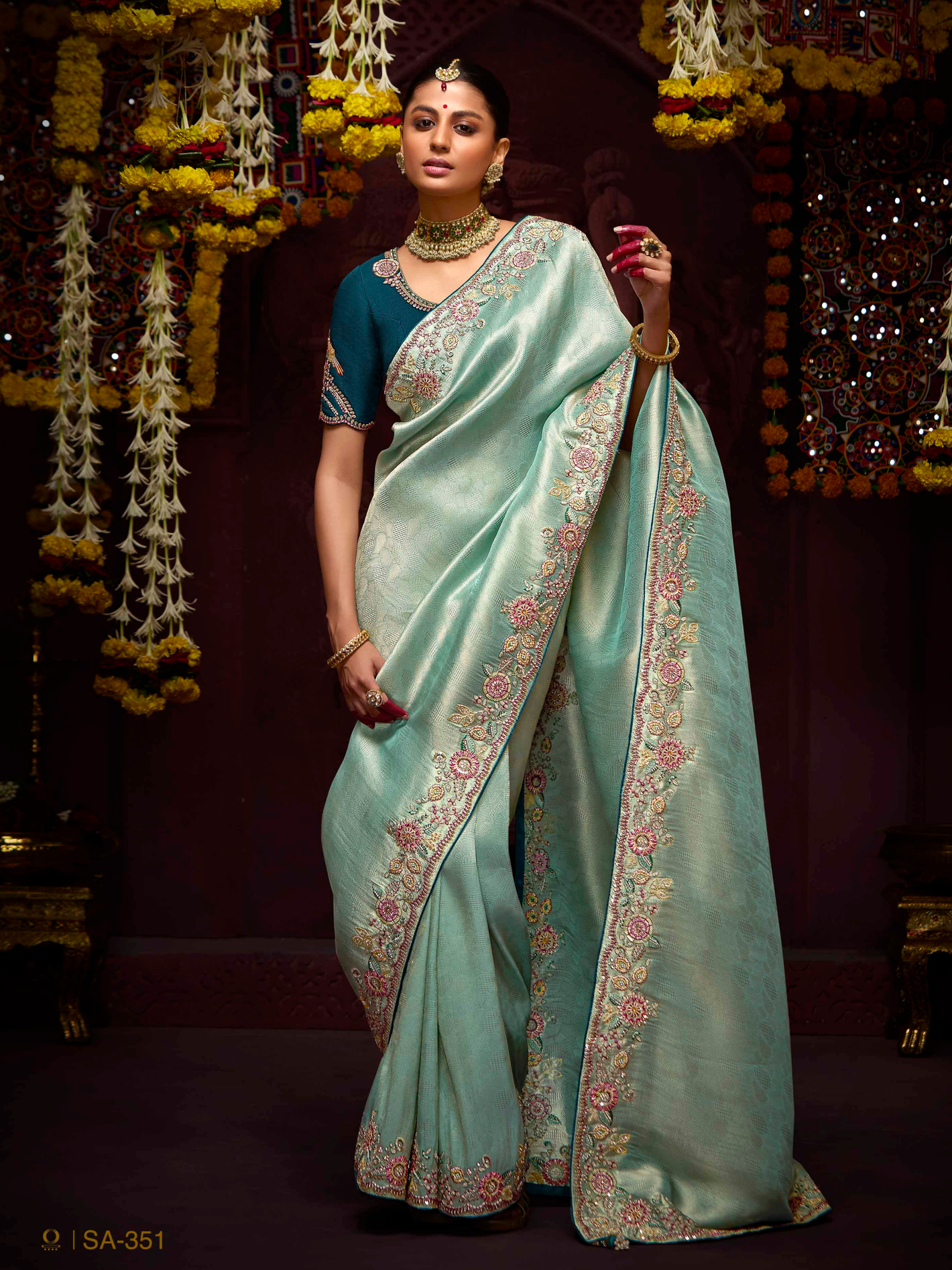 Woman in a light blue saree with floral patterns against a decorated background