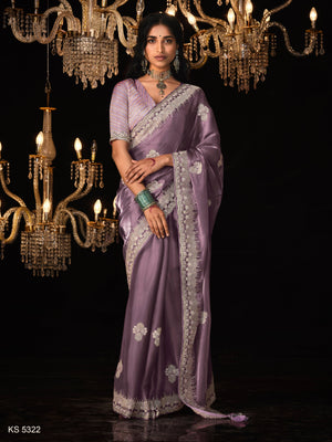 Woman in a lavender saree with intricate patterns standing in front of chandeliers.