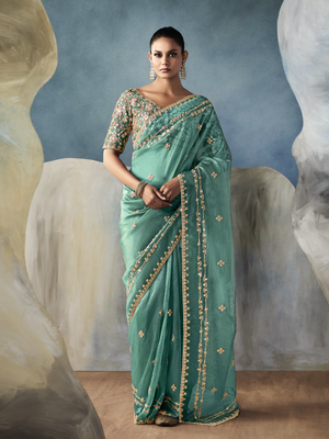 Woman wearing a green saree with gold embroidery against an abstract background