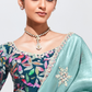 Woman wearing a traditional outfit with a floral blouse and light blue saree against a white background