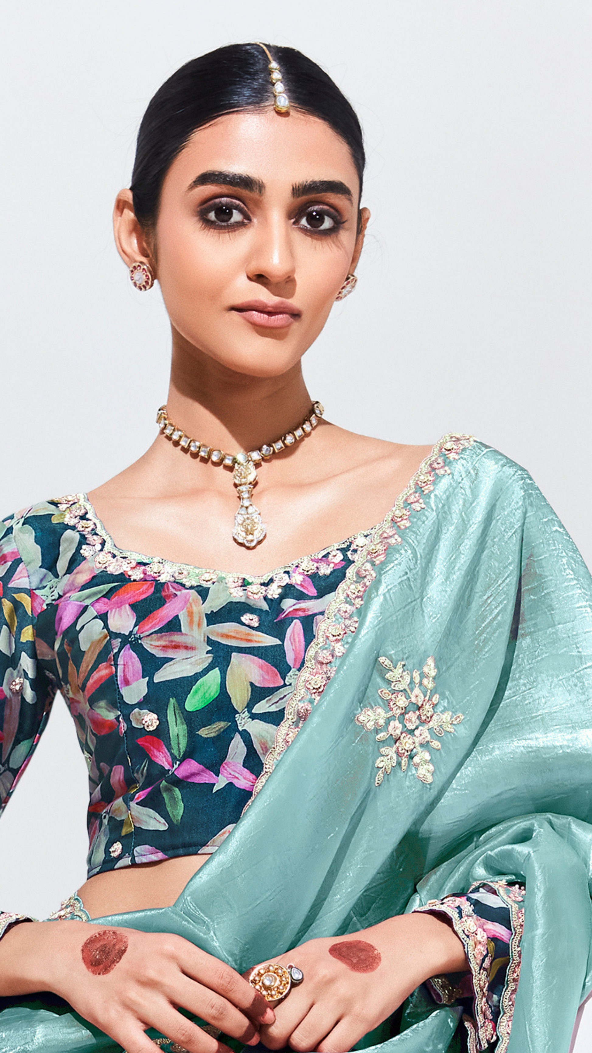Woman wearing a traditional outfit with a floral blouse and light blue saree against a white background