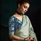 Woman wearing a blue floral blouse and light green saree against a dark background