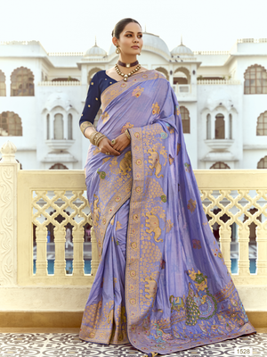 Woman in a traditional purple saree with gold patterns standing in front of an architectural building.