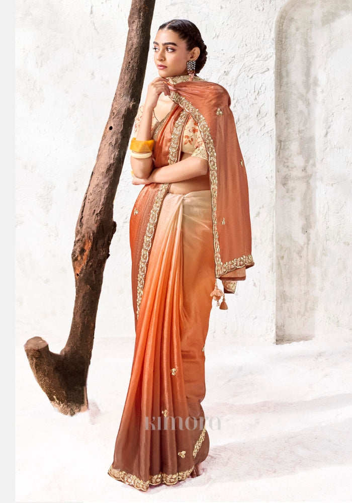 Elegant ombre designer saree in ivory and burnt orange with embroidered border, scattered floral motifs and silk tassels, perfect for weddings and festive celebrations.