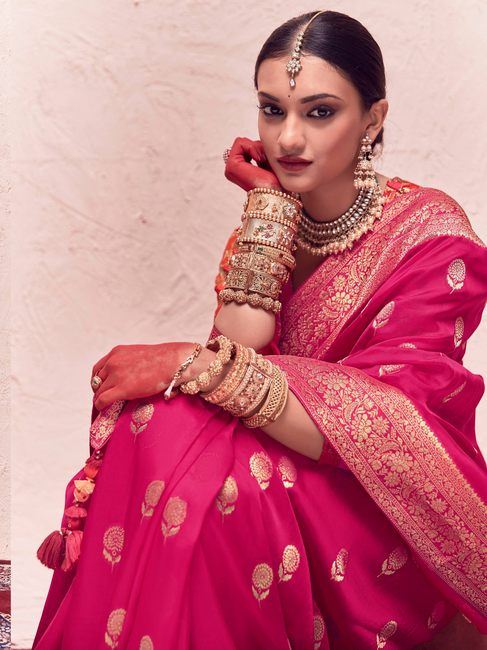 Woman in a pink traditional outfit with gold jewelry against a light background