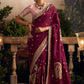 Woman in a maroon saree with gold embroidery standing outdoors, with 'Sindhuri' branding visible.